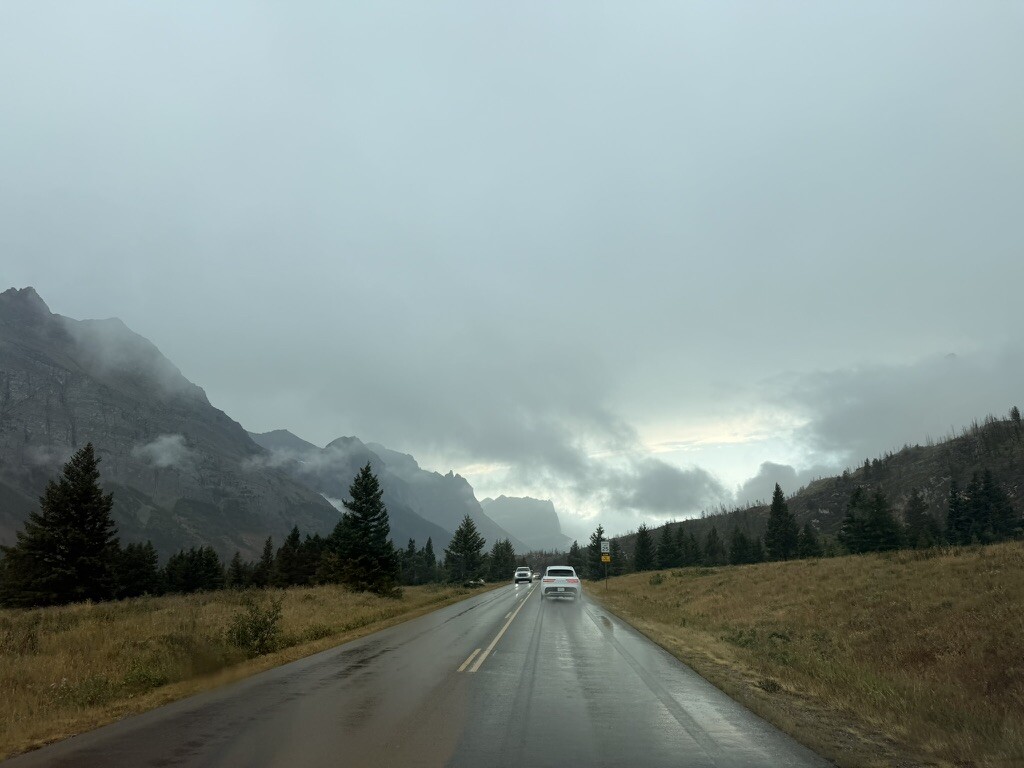 A wet road leading into low clouds at Many Glacier