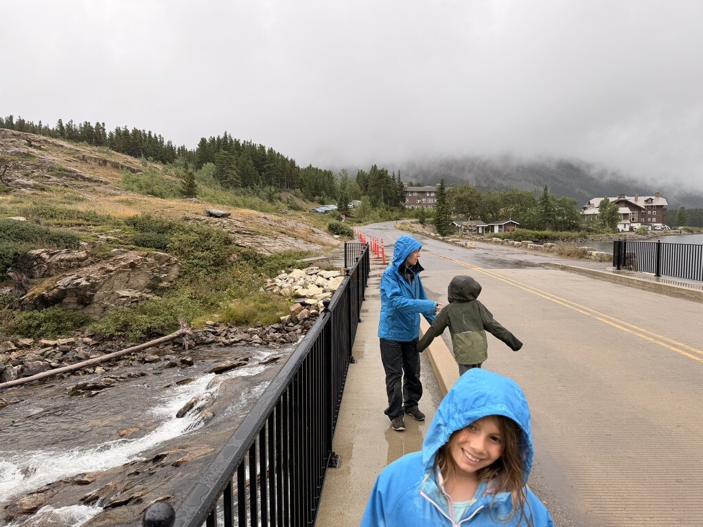 Family walking beside the rushing water in the rain at Many Glacier