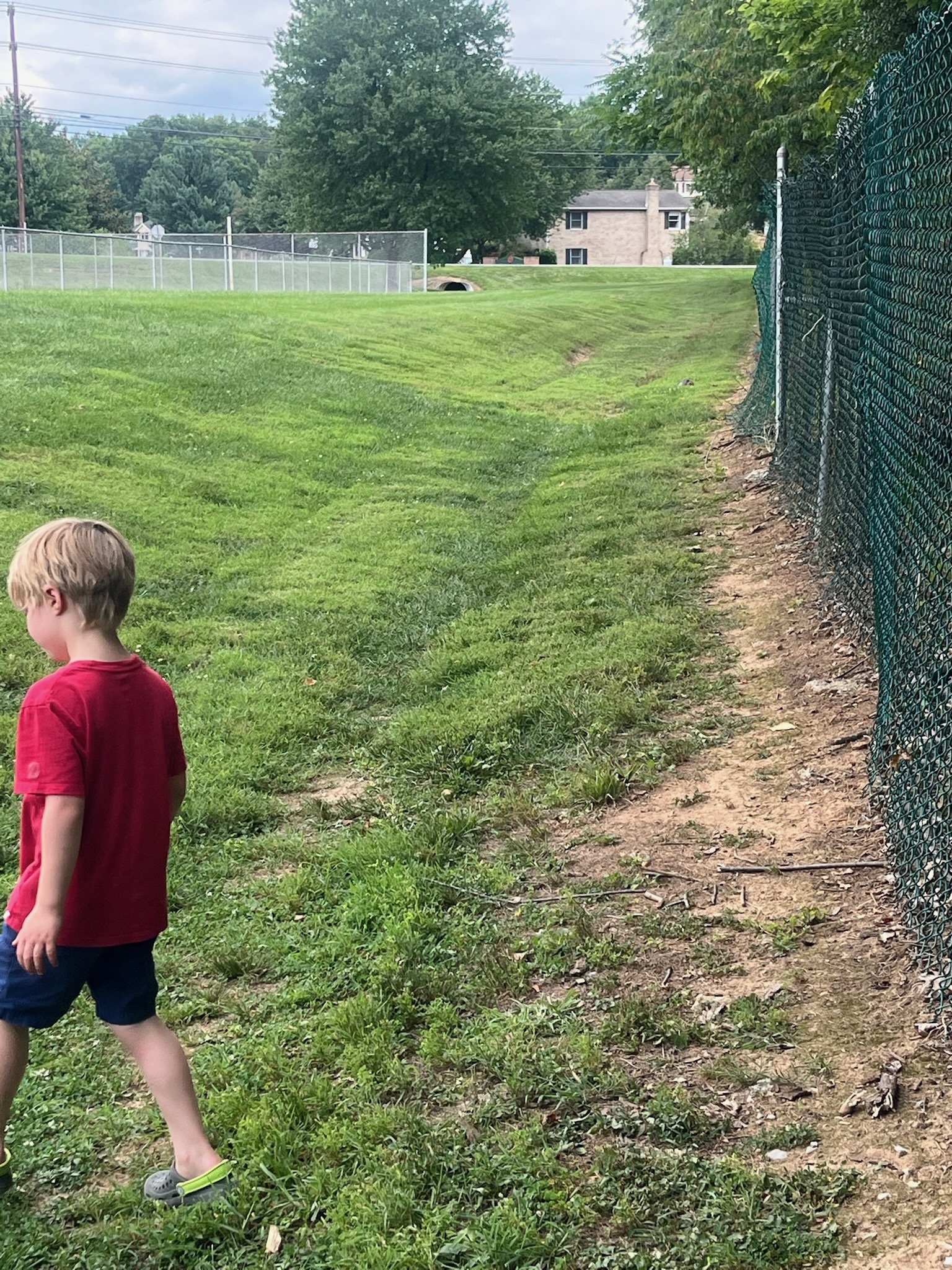 A child walking along a fence beside the park across from Emily's house